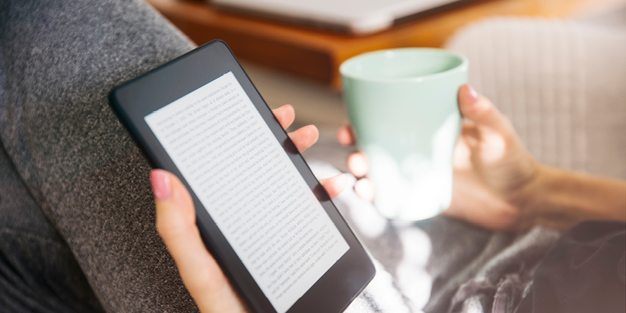 Tightly cropped image of a person's lap with a porcelain cup reading an e-book reader, OverDrive